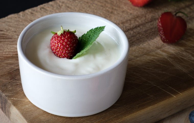 white bowl of plain yogurt with strawberry on top