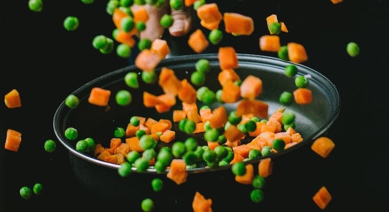 cut up carrots and peas flying out of a pan