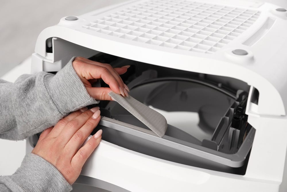 Litter-Robot base upside down with drawer removed and duct tape being peeled from the front edge of the waste port